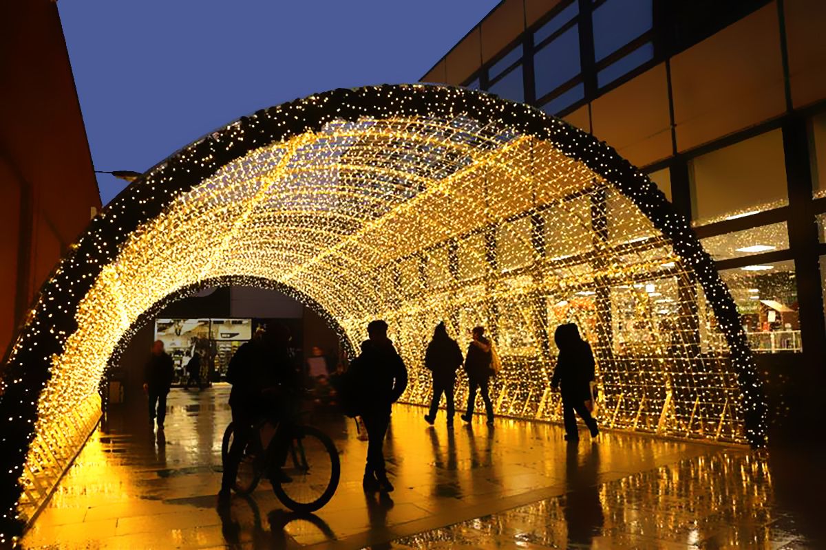 people walking and riding a bike under a tunnel of led lights installed outside between two buildings