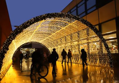 people walking and riding a bike under a tunnel of led lights installed outside between two buildings