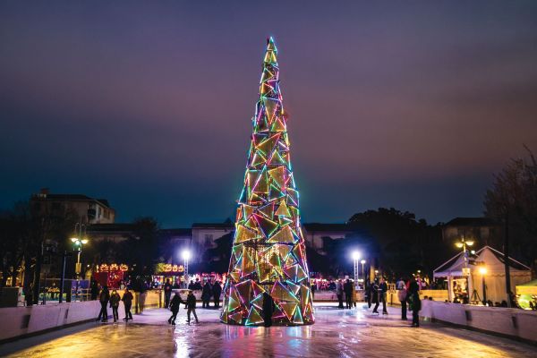 in the middle of an ice rink there's a big colourful christmas tree