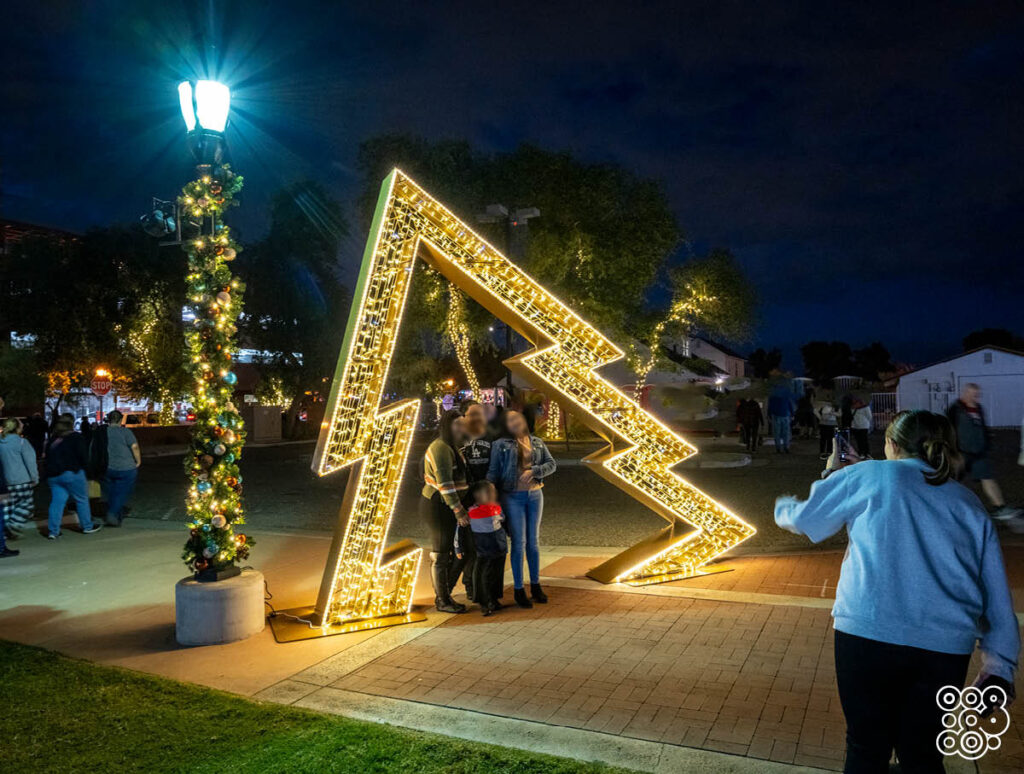 in the middle of a square there's a stylized lighting christmas tree with people inside that take pictures