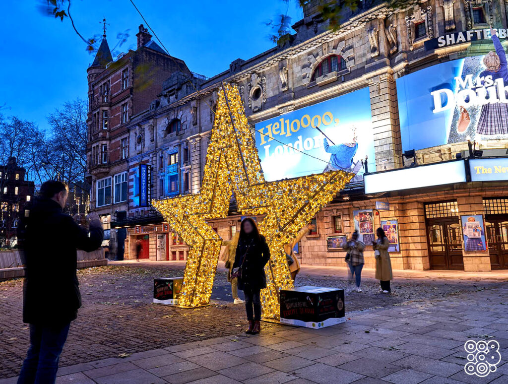 in front of a theatre there's a lighting 3d star with a woman that takes a picture